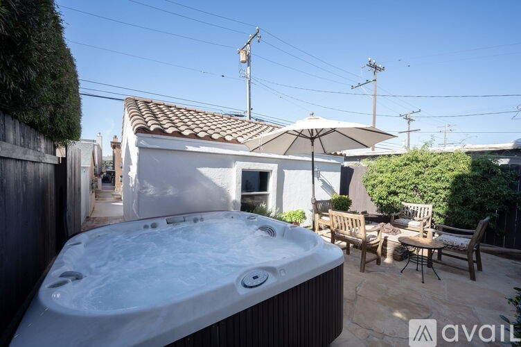 A hot tub is in the middle of a patio with chairs and an umbrella.