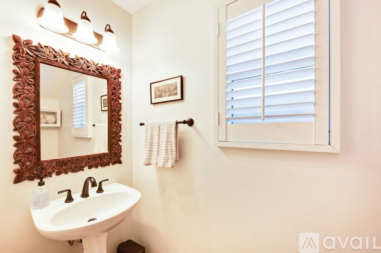 A bathroom with a white sink and a mirror with a leaf design.