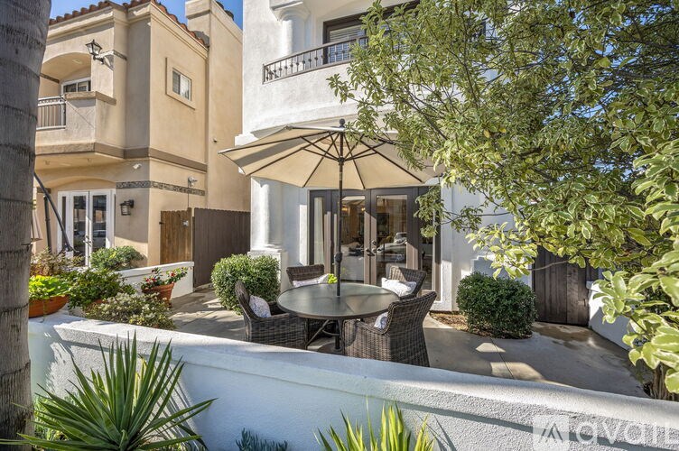 A patio with a table and chairs is surrounded by green plants.