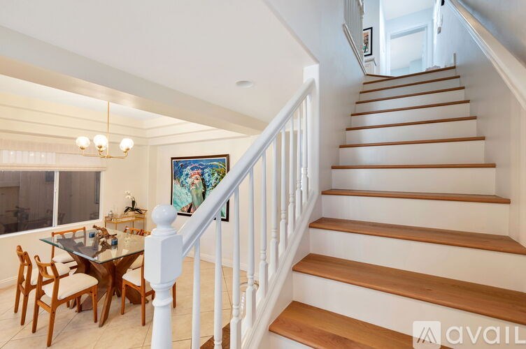 A staircase with wooden steps and white railings leads to a brightly lit room with a dining table and chairs.