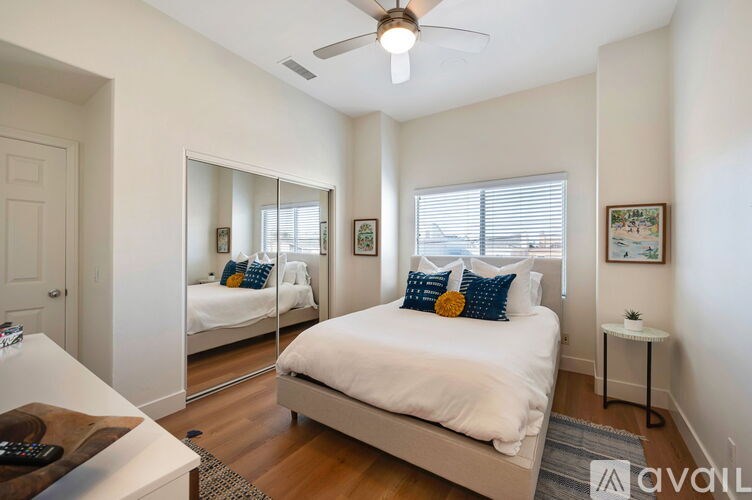 A bedroom with a bed, a mirror, a ceiling fan, and a small side table.
