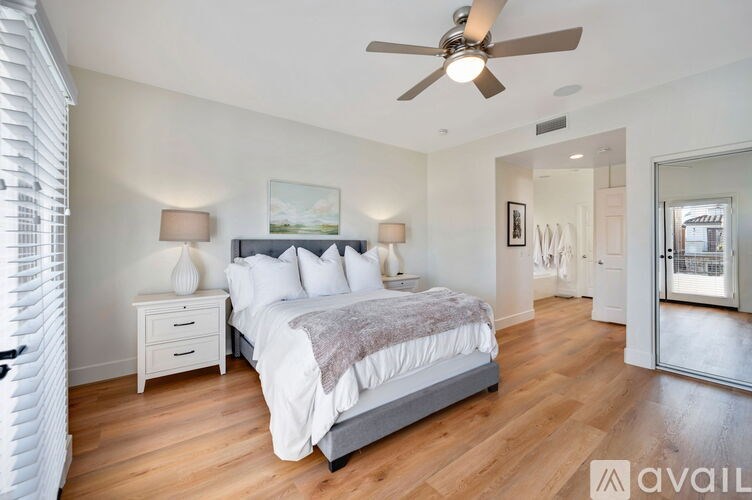 A bedroom with a large bed, a ceiling fan, and a painting on the wall.