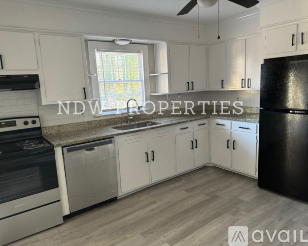 A kitchen with white cabinets and a black refrigerator is available for rent.