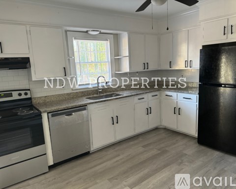 A kitchen with white cabinets and a black refrigerator is available for rent.