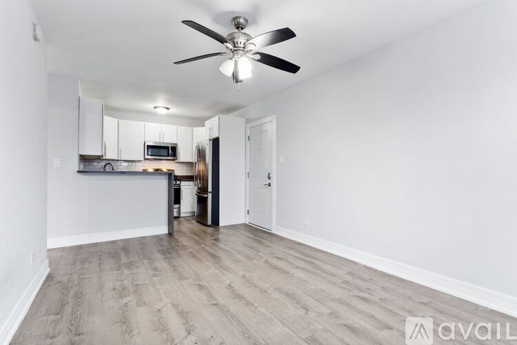 A spacious room with a ceiling fan and light fixture, featuring a kitchen area with white cabinets and a microwave.