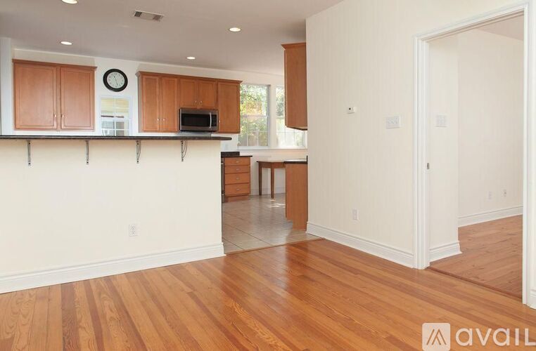 A kitchen with wooden floors and cabinets with a clock on the wall.