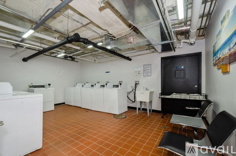A room with a white fridge, white cabinets, a black TV, and a black chair.