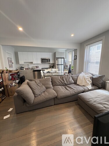 A living room with a grey couch and a kitchen in the background.