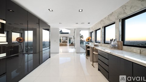 A modern kitchen with marble countertops and a large window overlooking a sunset.