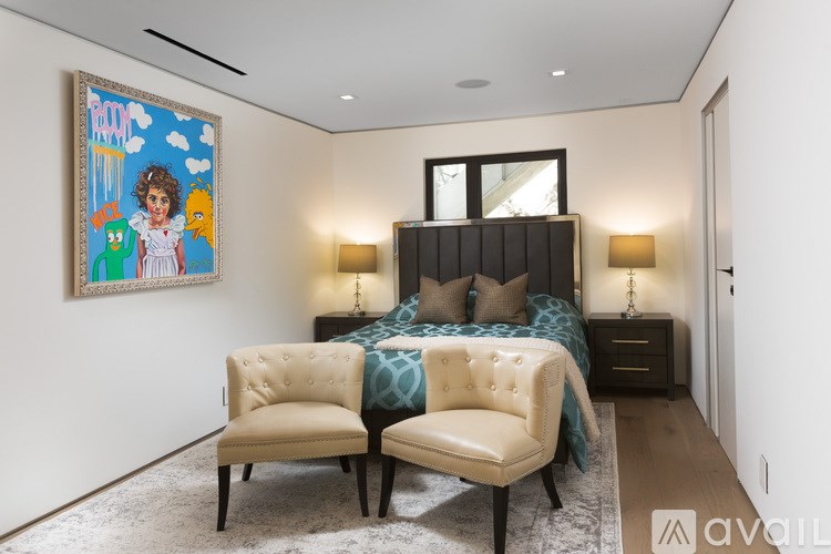 A bedroom with a bed, two chairs, and a painting on the wall.