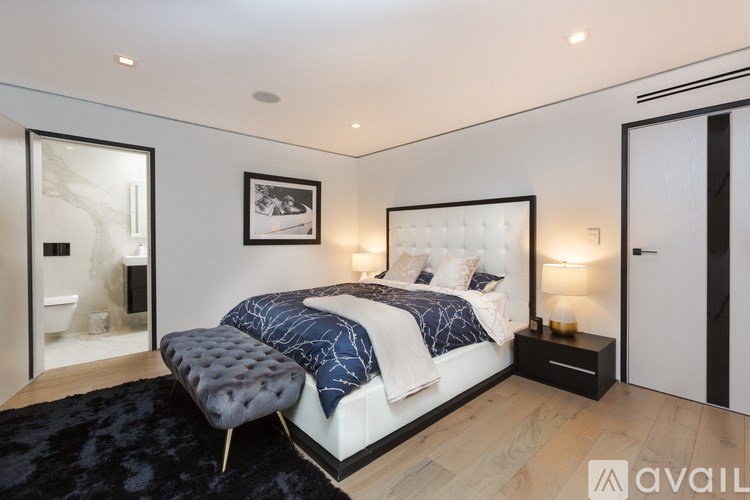 A modern bedroom with a large bed and a black ottoman.