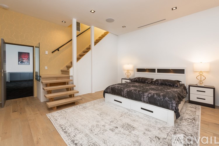 A bedroom with a bed, nightstand, and staircase.