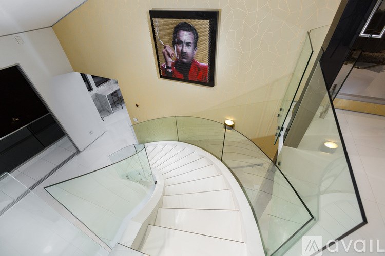 A spiral staircase with glass railings and a picture of a man in a red jacket hanging on the wall.