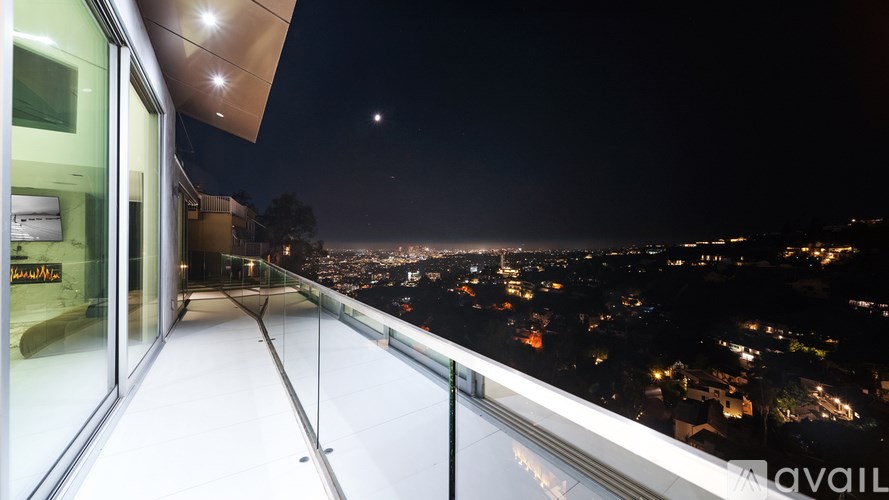 A balcony with a glass railing overlooking a city at night.