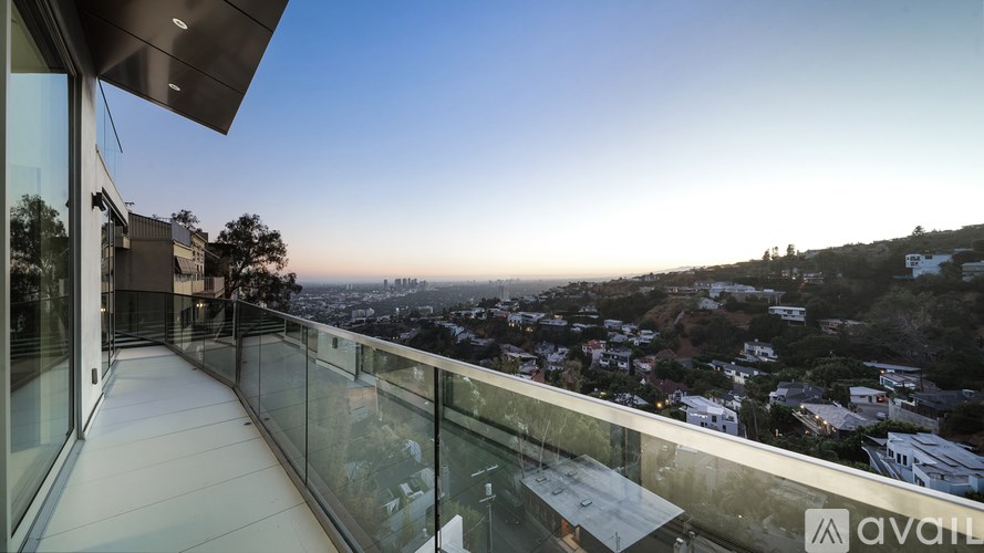 A balcony with glass railings overlooks a cityscape at dusk.