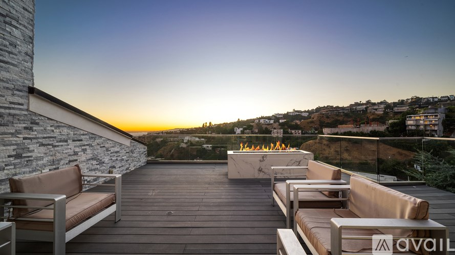 A patio with a stone wall and wooden decking with a sunset in the background.