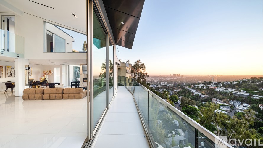 A modern house with a glass balcony overlooking a cityscape at sunset.