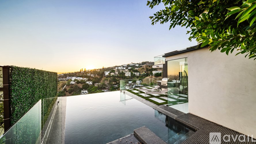 A modern house with a glass wall overlooking a pool and a view of the city.