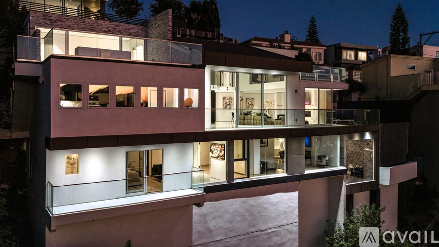 A modern house with a balcony and glass doors is illuminated at night.
