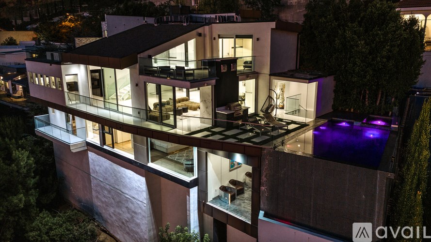 A modern house with a balcony and glass walls is illuminated at night.
