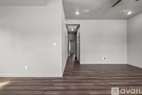 A room with wooden floors and white walls, with a hallway leading to a door.
