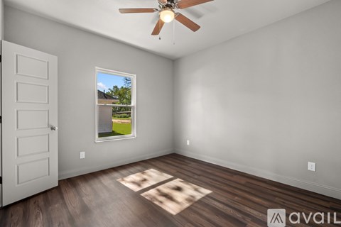 A room with a ceiling fan and a window showing a view of a house.