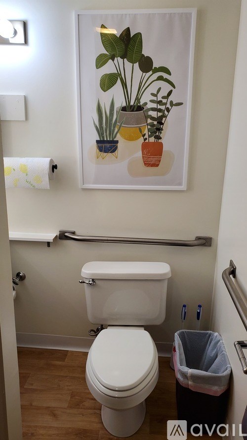 A white toilet in a small bathroom with a picture of plants on the wall.