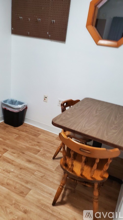 A wooden chair is in front of a white wall with a brown pegboard and a mirror.