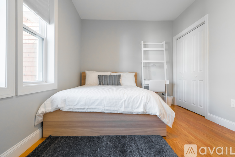 A bedroom with a white bed and a black rug.