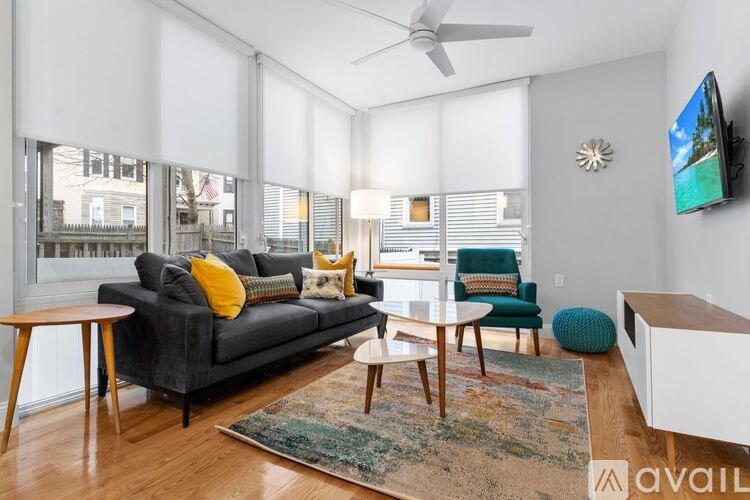 A living room with a grey couch, a green chair, a white coffee table, and a flat screen TV mounted on the wall.