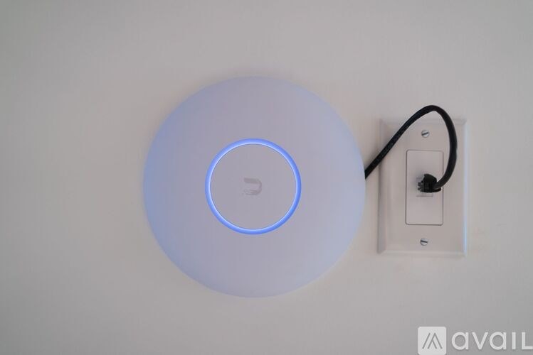 A white circular device with a blue light in the middle is plugged into a wall socket.