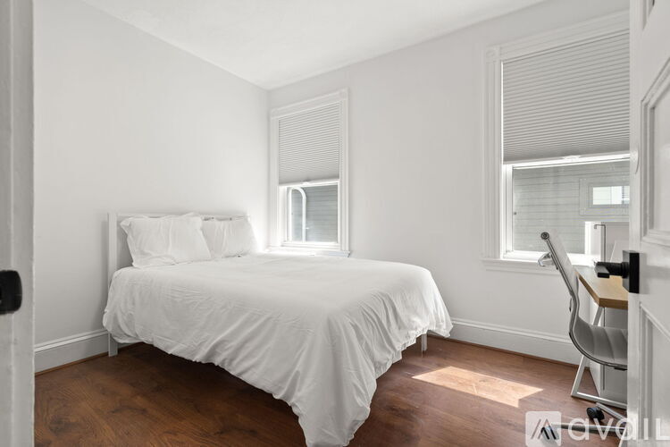 A white bedroom with a bed, chair, and window.