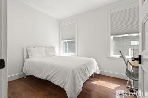 A white bedroom with a bed, chair, and window.