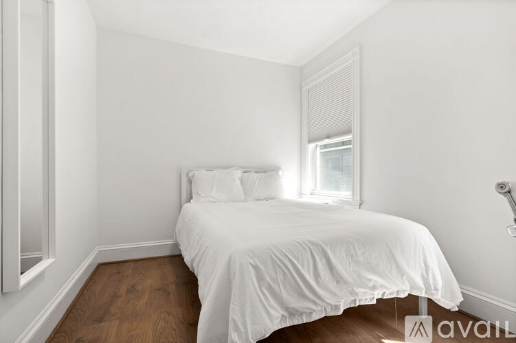 A white bed with a white comforter and pillow is in a room with white walls and a window.