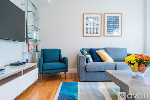 A living room with a blue couch, a blue chair, and a TV on the wall.