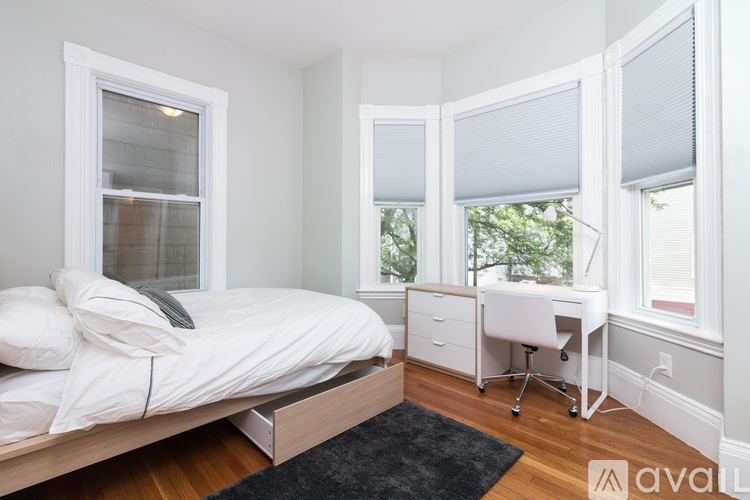 A white bedroom with a bed, nightstand and a cabinet.