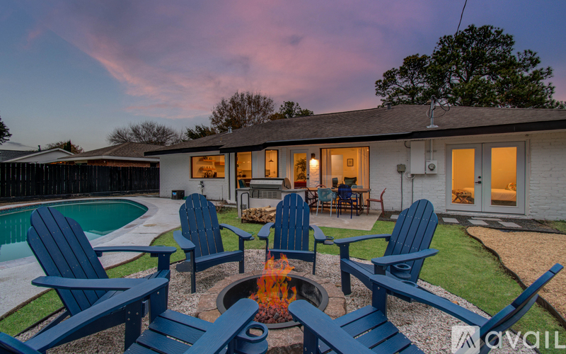 A house with a pool and four chairs around a fire pit.
