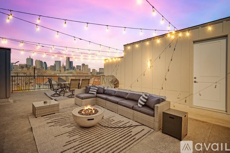 A patio with a couch, table, and a fire pit with string lights above.