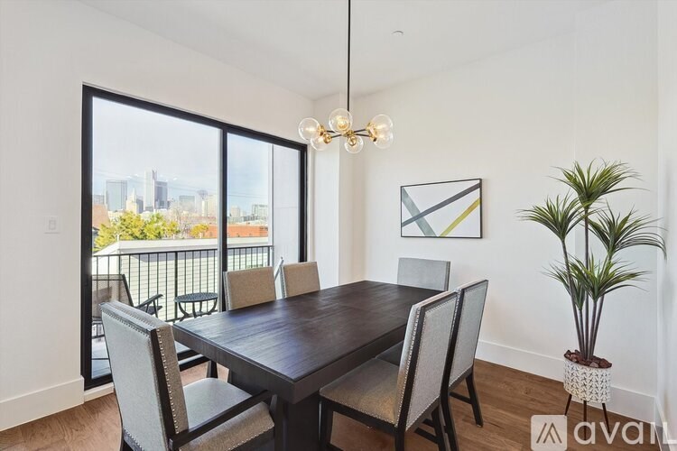A dining room with a wooden table and chairs, a potted plant, and a framed picture on the wall.