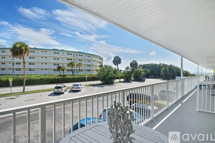 A balcony overlooks a road with cars and a white building with palm trees in the background.
