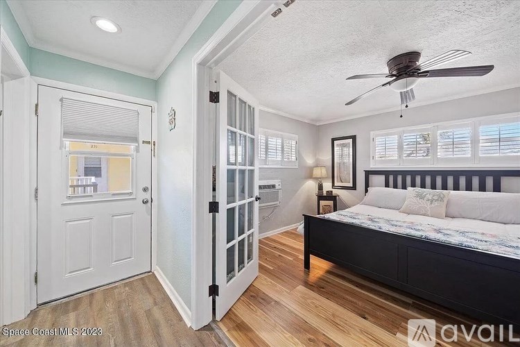 A bedroom with a bed, a ceiling fan, and a door leading to a balcony.