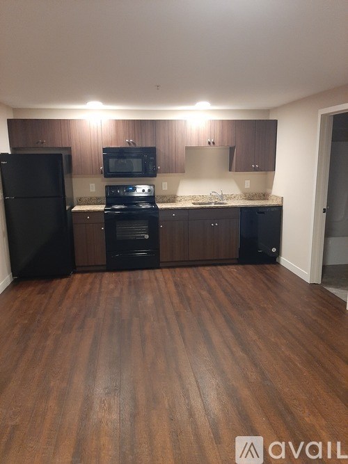 A kitchen with black appliances and wooden floors.
