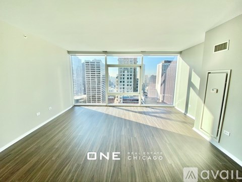 A spacious room with wooden flooring and a view of the cityscape outside the window.