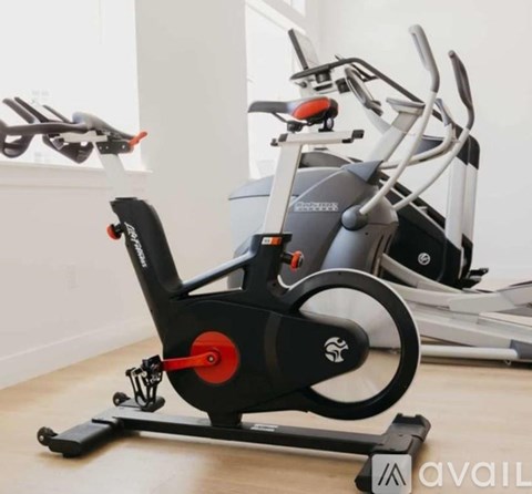 A stationary exercise bike with a black and red seat and handlebars is in a room.