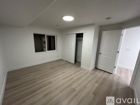 A room with wooden flooring and white walls, with a window and a door visible.