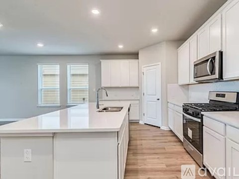 A kitchen with white cabinets and appliances, a large island, and a window with blinds.