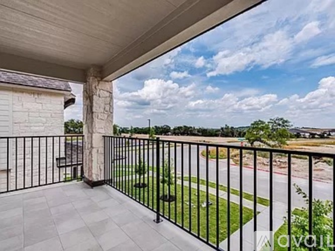 A balcony with a black railing and a view of a grassy area and a road.