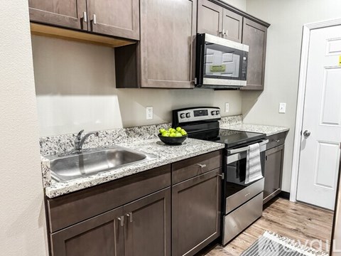 A kitchen with brown cabinets and a black microwave.