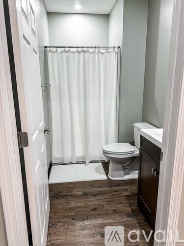 A white toilet sits in a small bathroom with a white shower curtain.