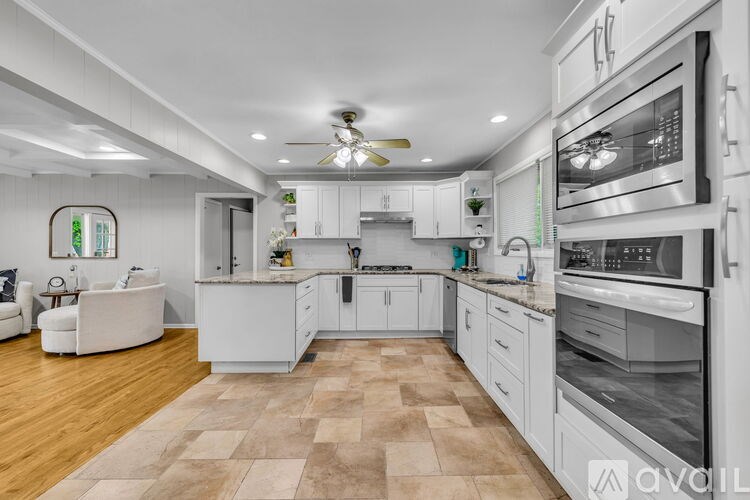 A modern kitchen with white cabinets and appliances, a ceiling fan, and a tiled floor.